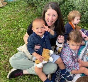Shalom Yeladim children with a teacher on a picnic blanket.